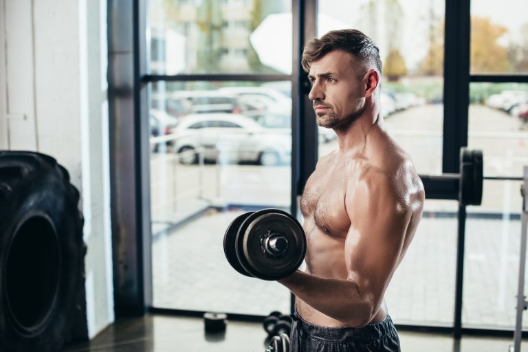 handsome shirtless sweaty sportsman training with dumbbells in gym